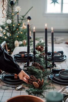 a table set for christmas with candles and pine cones