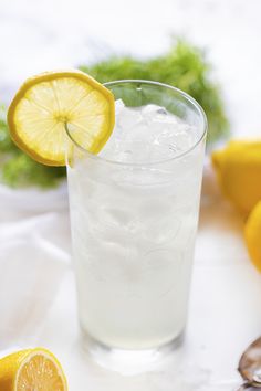 a glass filled with ice and lemons on top of a white table next to sliced lemons