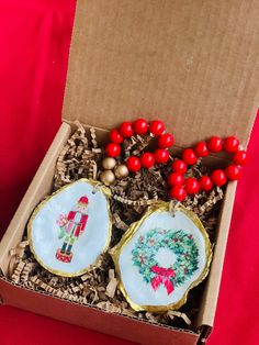 two christmas ornaments in a box on a red tablecloth with other decorations and items