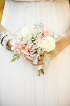 a woman in a white dress holding a bouquet of pink and white flowers on her arm