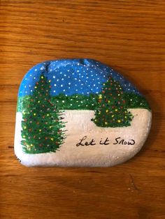 a painted rock that says let it snow with trees on the side and stars in the sky