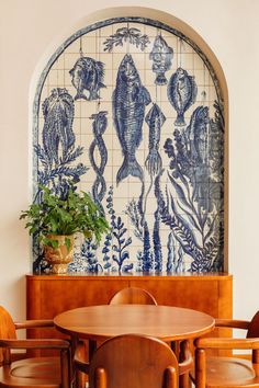 a dining table and chairs in front of a tile wall with fish design on it