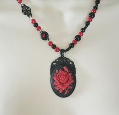 "Red Rose Necklace This beautiful necklace has red glass beads, black glass beads, seed beads, black metal connectors with rhinestones, black metal chain and a black metal pendant with resin rose. 20\" long. Lobster clasp." Gothic Beaded Jewelry Gift, Gothic Beaded Jewelry For Gift, Gothic Black Bead Necklace For Gift, Gothic Black Beads Necklace For Gift, Gothic Beaded Necklace For Gift, Antique Red Beaded Necklaces For Gift, Antique Red Beaded Necklace For Gift, Black Necklace With Rose Design As Gift, Black Necklace With Rose Design For Gift