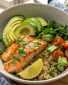 a bowl filled with salmon, rice and veggies next to sliced avocado