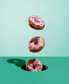 three donuts are flying in the air with sprinkles on them and one is pink