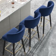 three green velvet bar stools in front of a marble countertop with gold legs