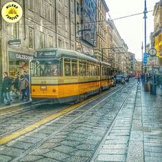 a yellow trolley is on the tracks in front of an old building and people are walking around