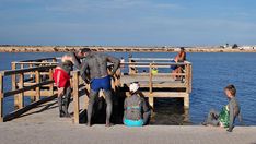 several people standing on a pier near the water and one person in wetsuits