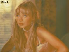 a woman with long blonde hair and blue eyes wearing a white dress in front of a window