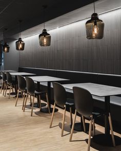 an empty restaurant with wooden tables and black chairs in front of a wall that has lights hanging from it