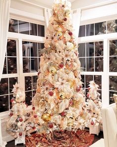 a white christmas tree with gold ornaments in front of a large window and windowsill