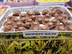 there are many trays of hats on display at this market stall, and one is filled with yellow flowers