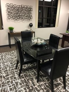 a glass table with black chairs in front of a wall mounted art piece on the wall