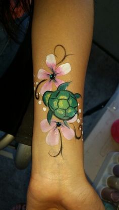 a woman's arm with a turtle and flowers painted on the back of it