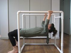 a woman is doing an exercise on a white metal frame in the middle of a room