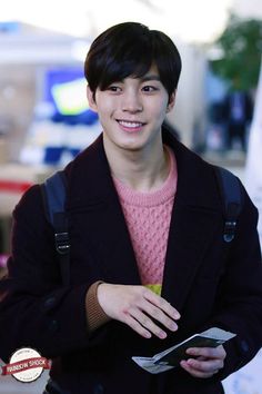 a young man in a pink sweater and black jacket is holding a cell phone while smiling at the camera