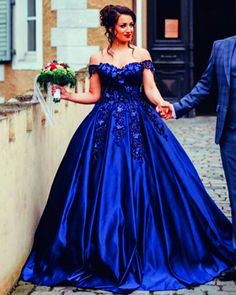 a man in a suit and woman in a blue dress walking down the street holding hands