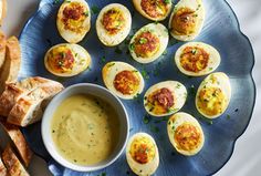 deviled eggs on a blue plate next to bread and dipping sauce in a bowl