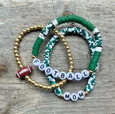 These are fun bracelets that are personalized perfectly for you! This stack is a set of {3} bracelets. The set includes two Heishi disc bracelets (the words can be changed) & a gold bracelet with a ball bead on it.  I change the bead color to match your school/team colors. I will also change the 'football' bead to whichever sport you choose. These stacks can be personalized, and bracelets added. You can reach out to me with any questions or personalization ideas! If you want bracelets added, rea Diy Team Bracelets, Sports Teams Clay Bead Bracelets, Clay Bead Bracelet Ideas School Spirit, School Color Clay Bracelets, Football Bracelet Diy, Football Mom Bracelet, School Spirit Beaded Bracelets, Clay Bead Bracelet Ideas Football, Team Beaded Bracelets