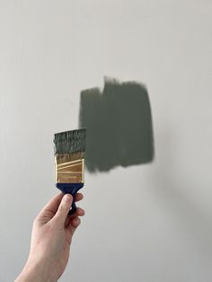 a hand holding a paintbrush with a green and gold stripe painted on the wall