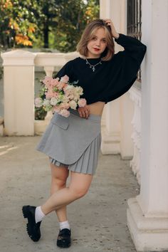 a woman wearing a skirt and black top posing for the camera with flowers in her hand