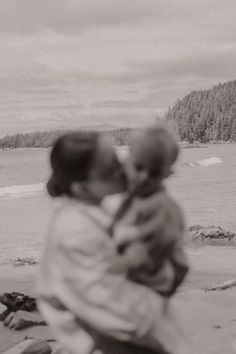 two people are hugging on the beach with trees in the background