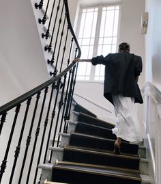 a woman is walking down the stairs with her hand on the railing and looking at the window