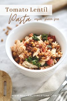 a white bowl filled with pasta and vegetables on top of a table next to utensils