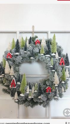 a christmas wreath hanging on the side of a door with red barns and evergreen trees