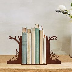 two books are sitting on a shelf next to a vase with flowers in it and one is shaped like a tree