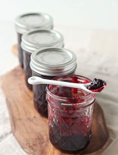 jars filled with jam on top of a wooden cutting board next to a white spoon