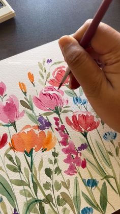 a person is holding a pencil in their hand and painting flowers with watercolors