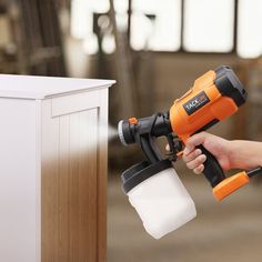 a person is holding a paint sprayer and spraying it on the side of a cabinet