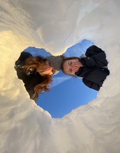 two people standing in the middle of a snow covered heart shaped hole, looking up into the sky