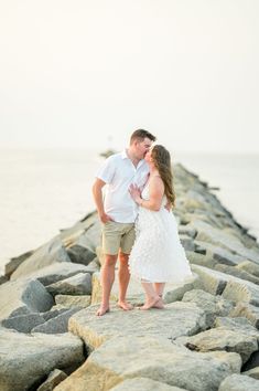 a man and woman standing on rocks near the ocean kissing each other in front of the water