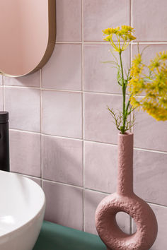 a pink vase with yellow flowers in it next to a white sink and wall mounted mirror