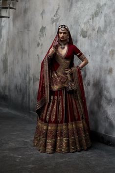 a woman in a red and gold bridal gown standing next to a gray wall