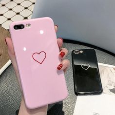 a woman holding up a pink phone case with a heart on it and another black one behind her