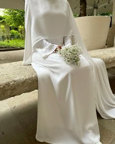 a woman sitting on a bench wearing a white dress and holding a flower in her hand