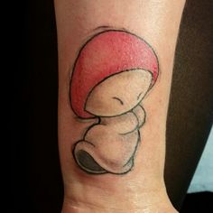 a small tattoo on the wrist of a person wearing a red hat with a mushroom on it