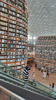 people are walking up and down an escalator in a library filled with books