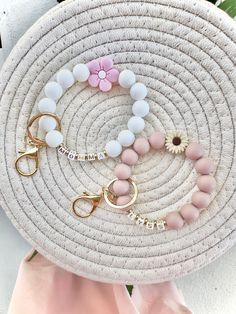 three bracelets with flowers on them sitting on top of a white platter next to a pink scarf