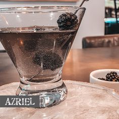 a glass filled with liquid sitting on top of a table next to a bowl of berries