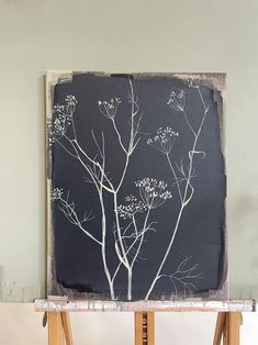 an easel with a painting on it sitting in front of a gray wall and white tree