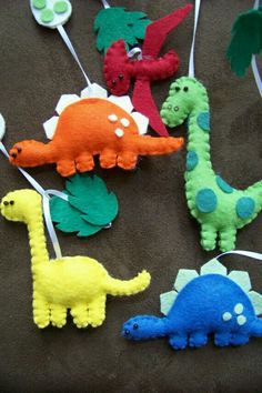 felt dinosaurs are hanging from strings on a brown surface with green, orange, and blue ones