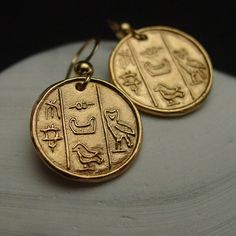 two gold coin earrings with egyptian writing on the front and back of each earring