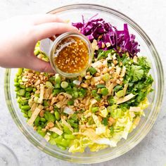 someone adding dressing to a salad in a glass bowl with lettuce, carrots and other vegetables