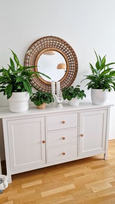 a white dresser topped with lots of potted plants and a round mirror above it