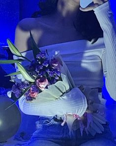 a woman holding a cell phone in her right hand and wearing a white top with flowers on it