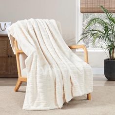 a white blanket sitting on top of a wooden chair next to a potted plant